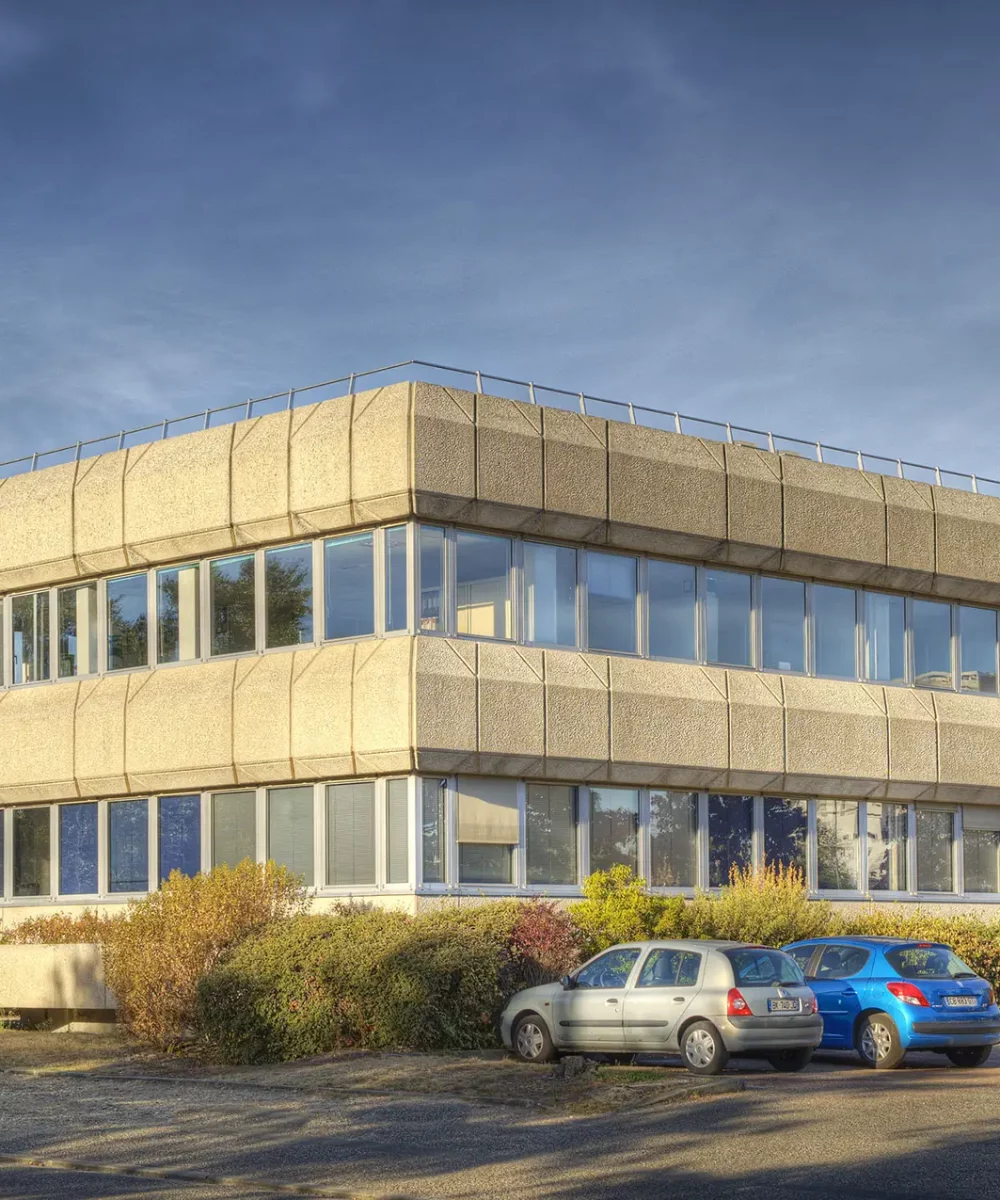 Modern beige concrete office building with stacked, angular upper levels and large windows against a blue sky